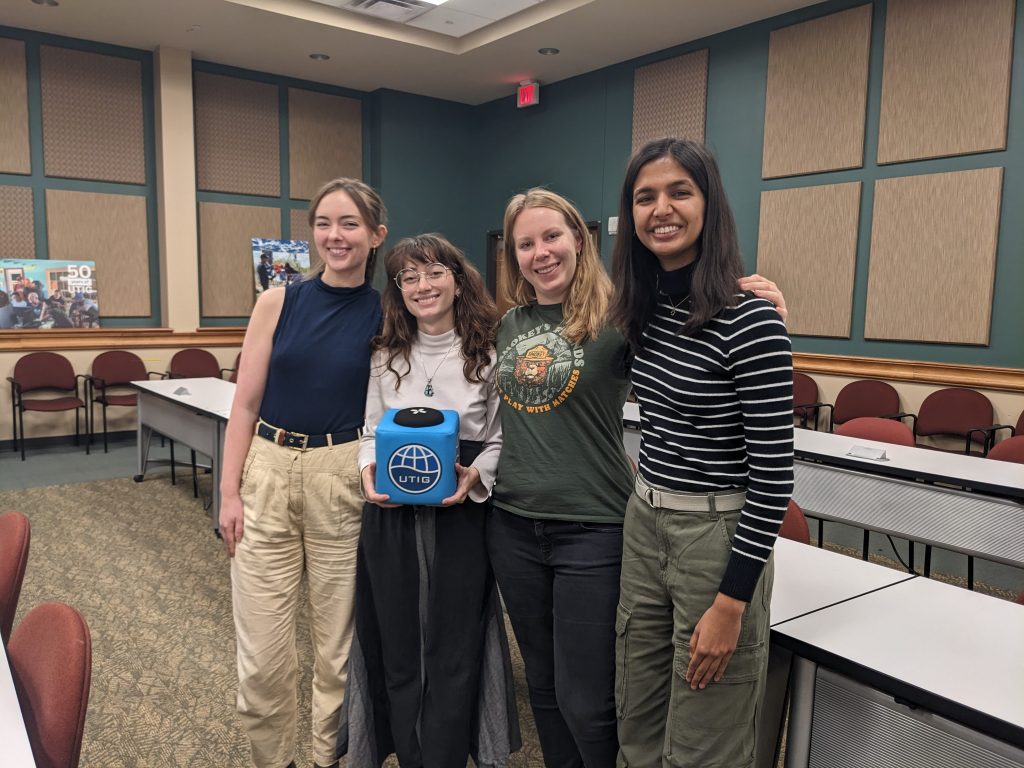 Photo of McKenzie, Mercedes, Julia, and Medha, pictured from left to right in the seminar room. Mercedes holding the UTIG Cube of Truth.