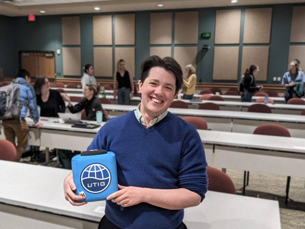 Photo of Spencer holding the UTIG Cube of Truth in the UTIG seminar room.