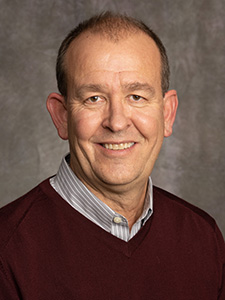 Portrait photo of Jim wearing a stripped shirt and a burgundy sweater.