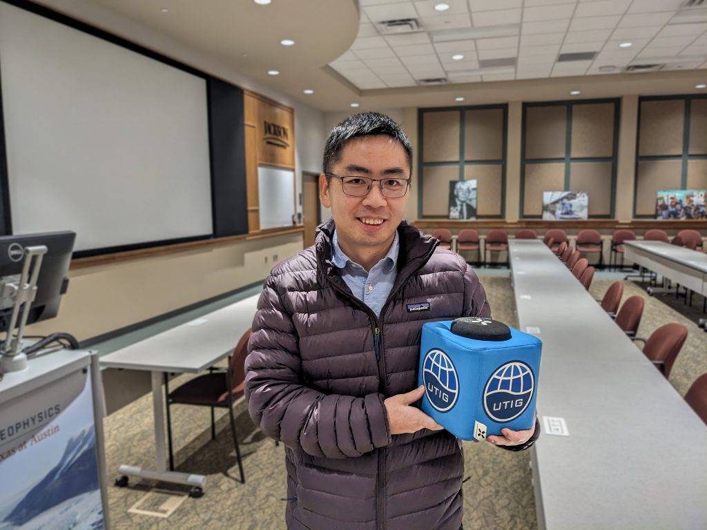 Photo of Wenbo holding the UTIG Cube of Truth in the UTIG seminar room.