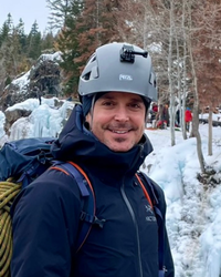 Portrait photo os Jesse in front of a mount of snow. He is wearing a gray helmet and a blue jacket.