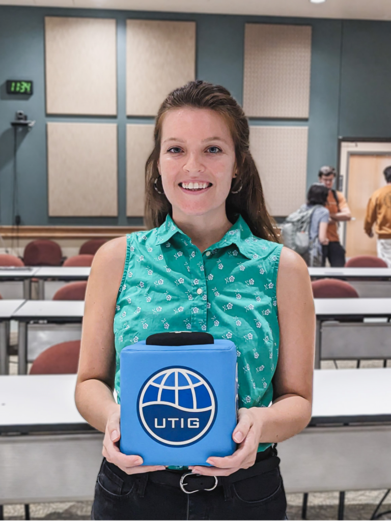 Photo of Perianne, holding the UTIG cube of truth in the UTIG seminar room.