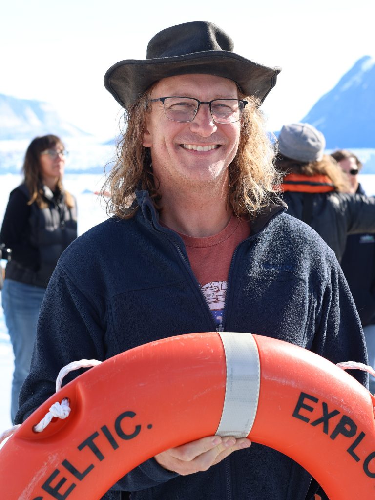 Photo of Sean. He is wearing a hat, and is holding an orange safety ring float.