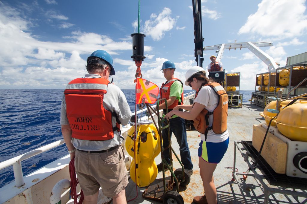 Researchers Peter Lemmond (left), David DuBois (middle) and Jenny Harding (right) prepare an ocean-bottom seismometer (OBS) ready to be dropped over the side of the R/V Marcus Langseth.